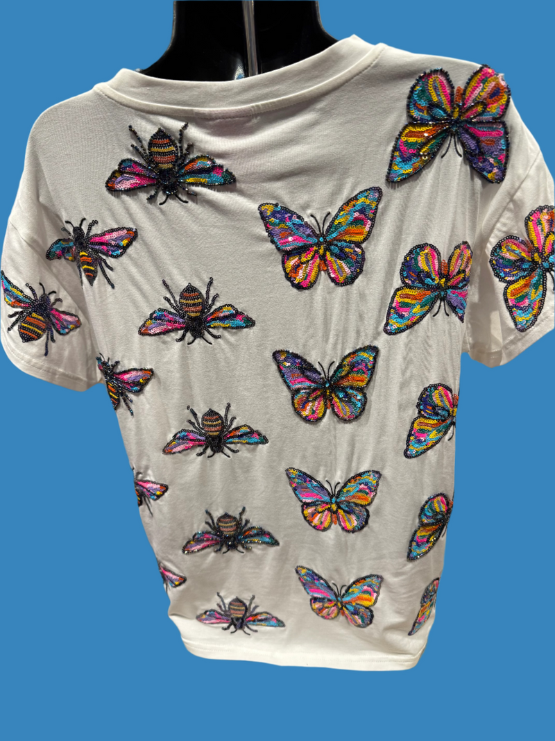 White t-shirt with colorful butterfly and bee designs on a chair.