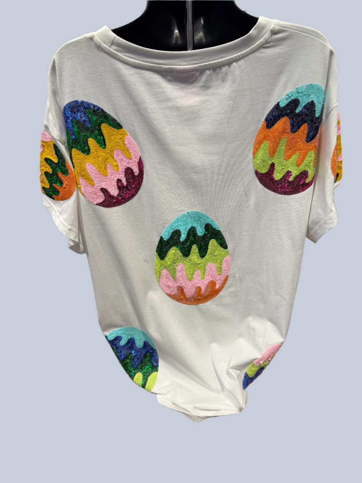 White sweater with colorful egg designs on a mannequin in a store setting.