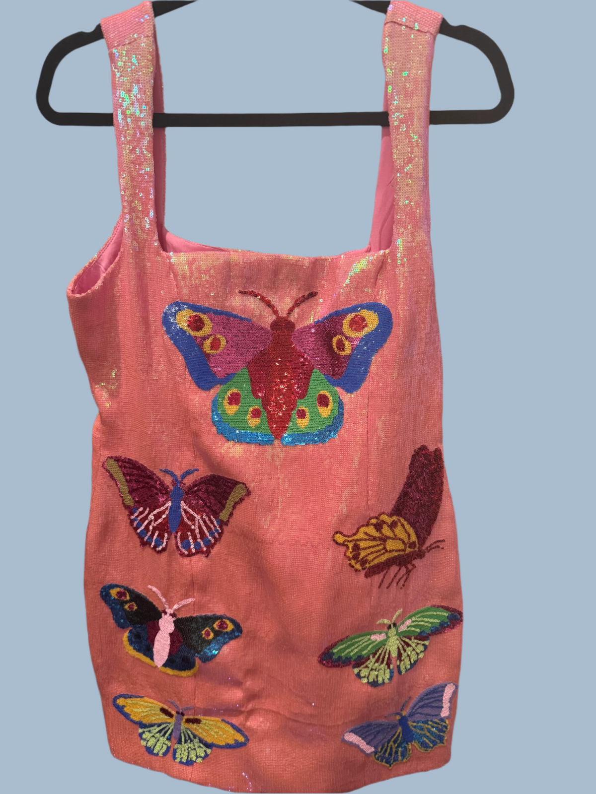 Pink dress with butterfly designs on a hanger against a white wall.